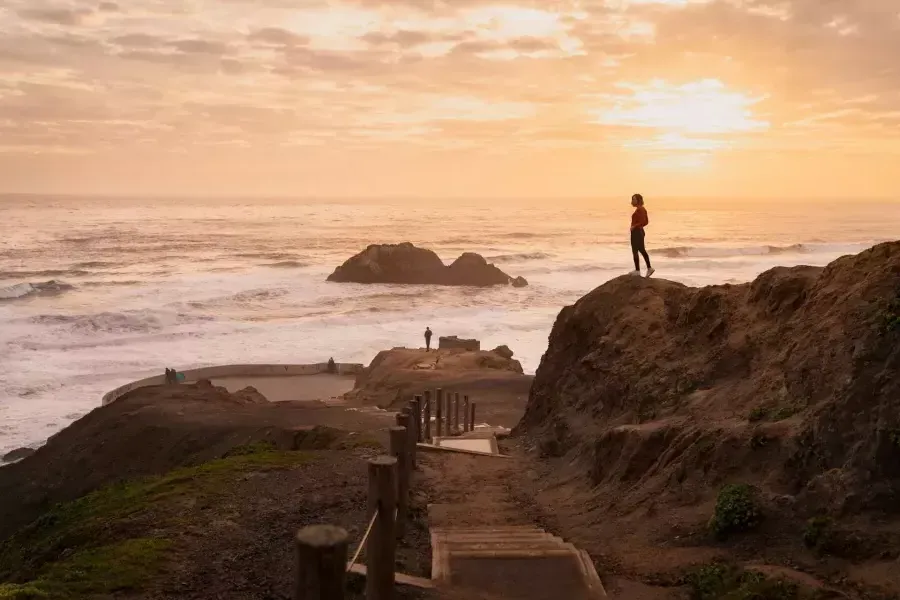 Dos personas están de pie sobre rocas con vistas al océano en Sutro Baths en San Francisco.